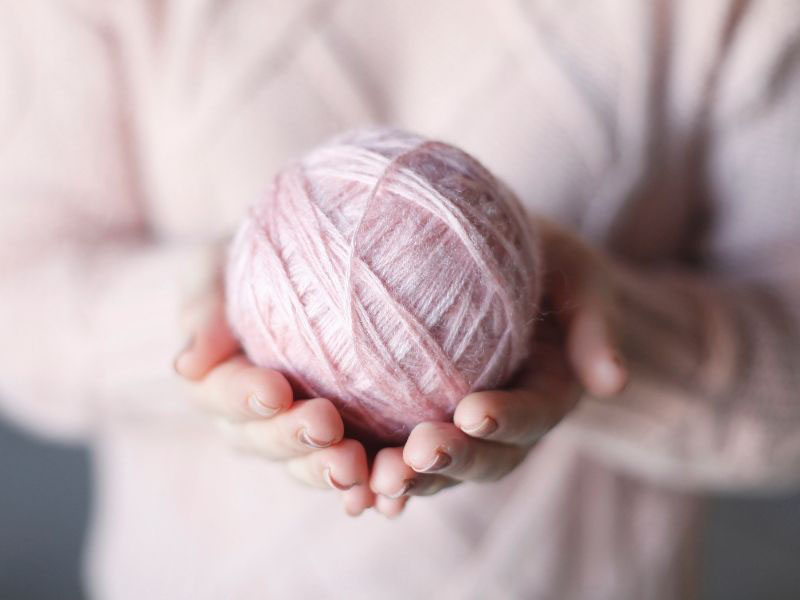 A person holding a pink ball of yarn.