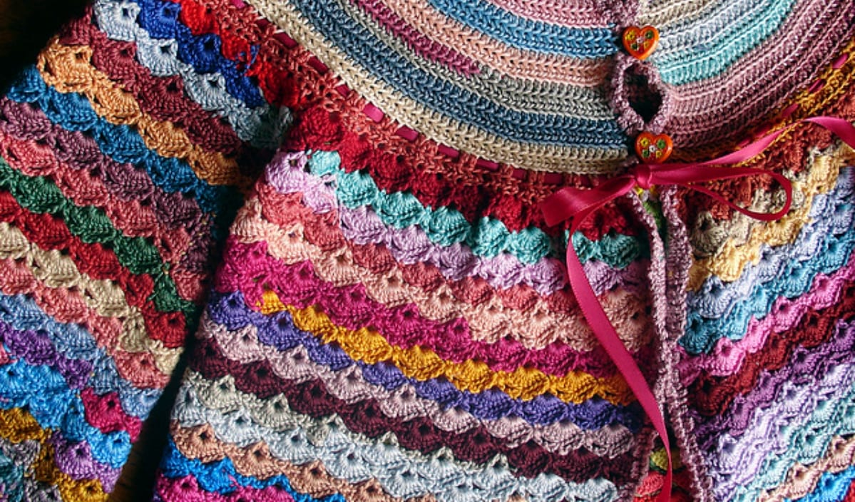 This adorable crocheted baby cardigan showcases colorful scalloped patterns and a ribbon tie, complete with two heart-shaped buttons. Perfect for those looking for free crochet patterns to craft something unique.