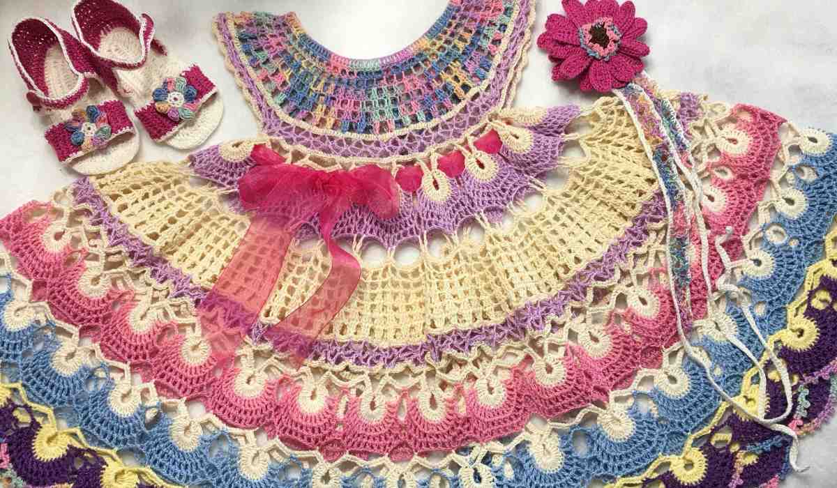 Colorful crocheted baby outfit with a multi-layered Baby Dress, matching sandals, a flower headband, and a top—all in pastel shades of pink, blue, purple, and cream.