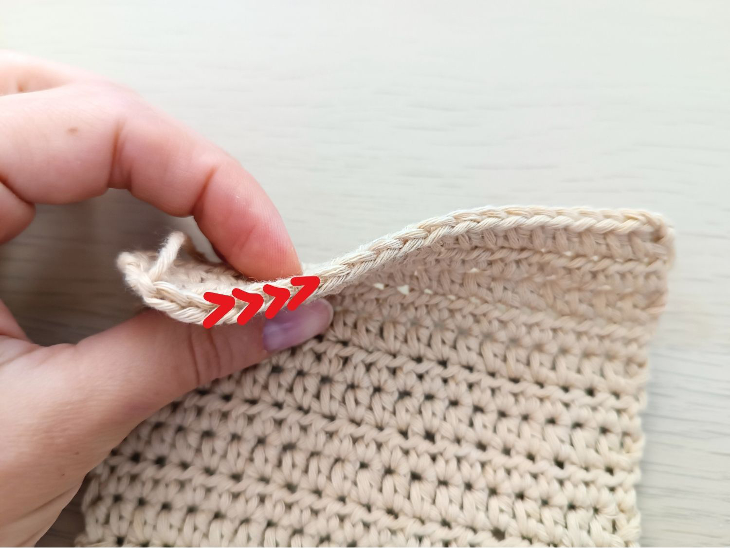 A person holding a crocheted bag with a red arrow.