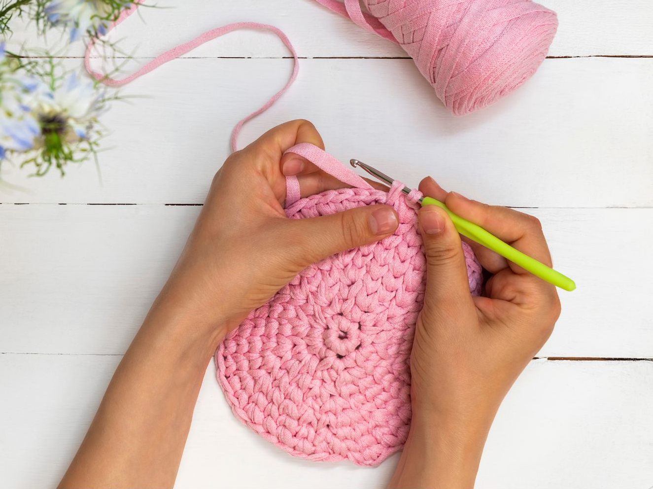 A person crocheting a pink crocheted bag on a wooden table.