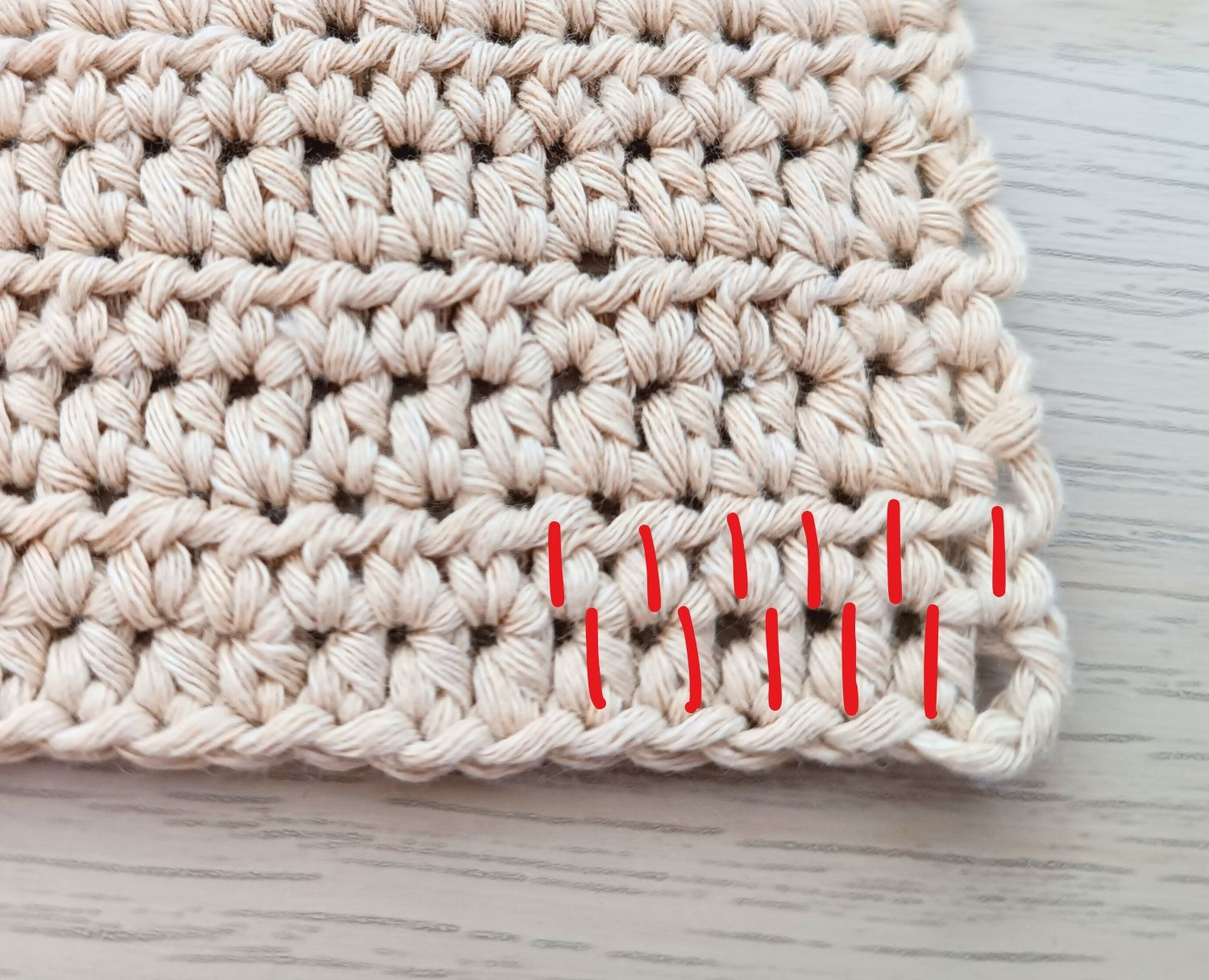 A crocheted square with two red threads on it.